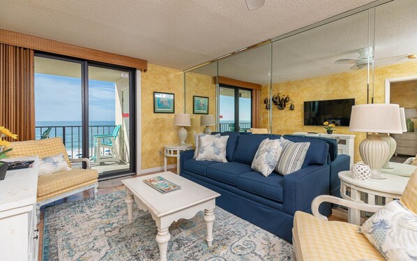 Ein Hotelzimmer mit Sofa, Sesseln, einem Couchtisch, einem Fernseher und einem Balkon mit Meerblick.