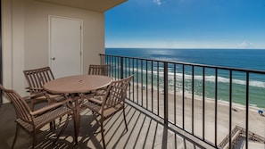 A balcony with a table and chairs, overlooking a beach with the ocean and a clear sky. - Phoenix Ii 2112 2 Bedroom Condo (Orange Beach)