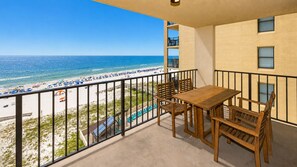 A balcony with a view of the beach, a wooden table, and chairs. - Phoenix Ii 2071 3 Bedroom Condo (Orange Beach)
