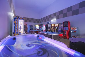 A pool table with a pool cue, surrounded by various arcade games in a room with checkered walls. - Phoenix Ii 2071 3 Bedroom Condo (Orange Beach)