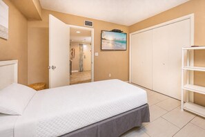 A bedroom with a bed, a wardrobe, a shelf, and a door leading to a bathroom. - Phoenix Ii 2071 3 Bedroom Condo (Orange Beach)