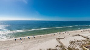 A beach with a wooden walkway leading to the water, and several blue umbrellas lined up on the sand. - Phoenix Ii 2128 3 Bedroom Condo (Orange Beach)