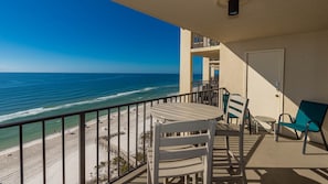 A balcony with a view of the beach and ocean, a table, two chairs, and a door. - Phoenix Ii 2128 3 Bedroom Condo (Orange Beach)
