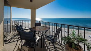 A balcony with a table and chairs, overlooking a beach and the ocean. - Phoenix Ii 2115 2 Bedroom Condo (Orange Beach)