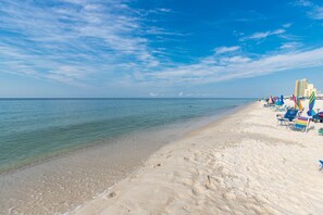 A beach with clear blue water, white sand, and a row of beach chairs and umbrellas. - Phoenix Ii 2124 1 Bedroom Condo (Orange Beach)
