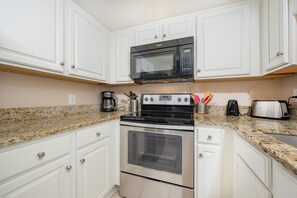 A kitchen with white cabinets, a black microwave, a stainless steel stove, a coffee maker, and a toaster. - Phoenix Ii 2092 2 Bedroom Condo (Orange Beach)