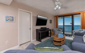 A living room with a television, a sofa, a coffee table, and a view of the ocean through a sliding door. - Phoenix Ii 2092 2 Bedroom Condo (Orange Beach)