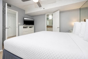 A bedroom with a large bed, a television, a ceiling fan, and a bathroom visible through an open door. - Phoenix Ii 2114 1 Bedroom Condo (Orange Beach)