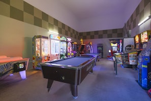 A room with a pool table, arcade games, and a checkered wall. - Phoenix Ii 2114 1 Bedroom Condo (Orange Beach)