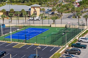 A multi-sport court with basketball and tennis courts, surrounded by a parking area and a building with a red roof. - Phoenix Ii 2047 2 Bedroom Condo (Orange Beach)