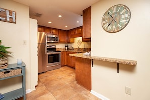 A kitchen with wooden cabinets, stainless steel appliances, a granite countertop, and a wall clock. - Phoenix Ii 2047 2 Bedroom Condo (Orange Beach)
