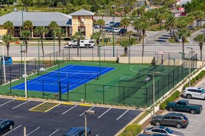 A multi-sport court with basketball and tennis courts, surrounded by a parking area and a building with a red roof. - Phoenix Ii 2022 2 Bedroom Condo (Orange Beach)