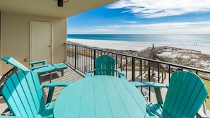 Un balcon avec des fauteuils Adirondack turquoise et une vue sur la plage.