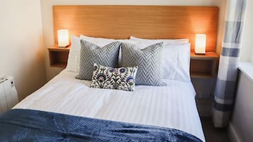 A hotel room with a wooden headboard, white bedding, two nightstands with lamps, and a blue blanket on the bed.