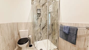 A bathroom with a glass-enclosed shower, a toilet, and a towel rack with a towel.