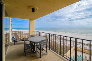 A balcony with a table and chairs, overlooking a beach with a railing. - Phoenix Ii 2048 3 Bedroom Condo (Orange Beach)