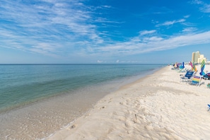 A beach with clear blue water, white sand, and a row of beach chairs and umbrellas. - Phoenix Ii 2107 2 Bedroom Condo (Orange Beach)