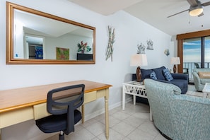 A living room with a wooden desk, a chair, a sofa, and a large mirror. - Phoenix Ii 2024 1 Bedroom Condo (Orange Beach)