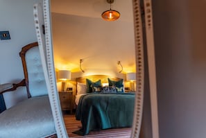 Una habitación de hotel con una cama, lámparas de noche y un espejo que refleja el cuarto.