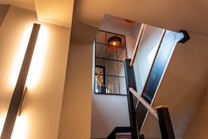 Una escalera con barandilla, un aplique de pared y una ventana que da al interior.
