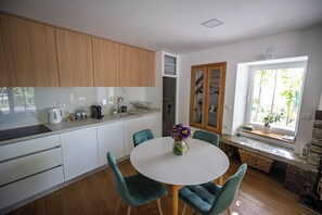 A modern kitchen with white cabinets, a round dining table, teal chairs, and a window with a view of greenery.