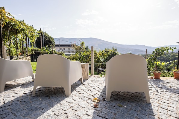 A patio with stone flooring, two beige chairs, and potted plants.
