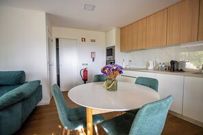 A modern kitchen with wooden cabinets, a white countertop, and a vase with flowers on a round table.