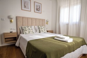 A hotel room with a bed, two nightstands, a wooden dresser, and a window with sheer curtains.