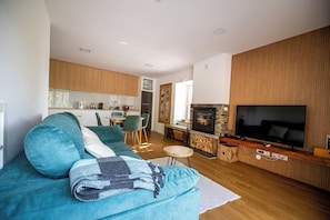 A modern living room with a sofa, a television, and a kitchen in the background. - Quinta do Passal - Country House (Parada de Ester)