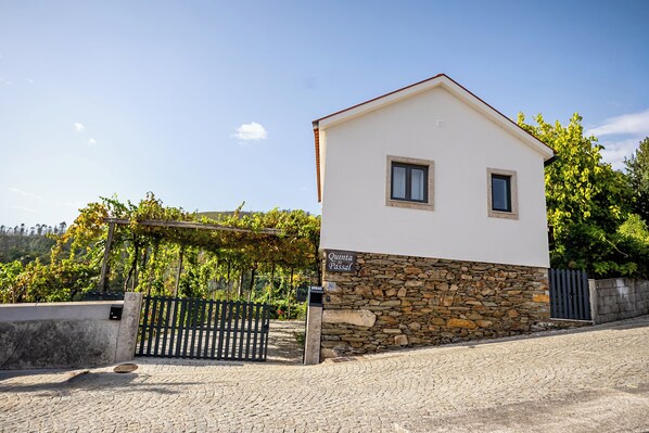 A small, single-story building with a stone foundation and a white upper section. There is a sign on the building that reads 'Quinta do Passal.'