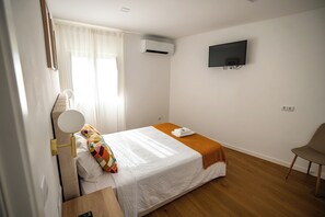 A hotel room with a bed, a TV mounted on the wall, a chair, and a bedside table with a lamp.