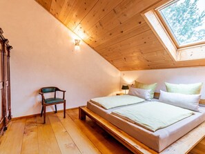 A room with a sloped ceiling, wooden beams, a bed with two pillows, a chair, and a small table with a lamp. - Mayrhof - Mountain View (Eggstatt)