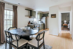 Una cocina moderna con armarios oscuros, una mesa de comedor con sillas y vistas al exterior por una ventana.