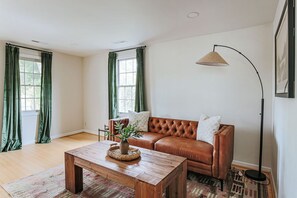 A living room with a brown leather sofa, a wooden coffee table, and a floor lamp. - The 1st Street Bungalow (Charlottesville)