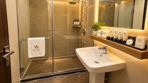 Un baño moderno con cabina de ducha de vidrio, un lavabo blanco y un mueble de tocador con artículos de aseo.