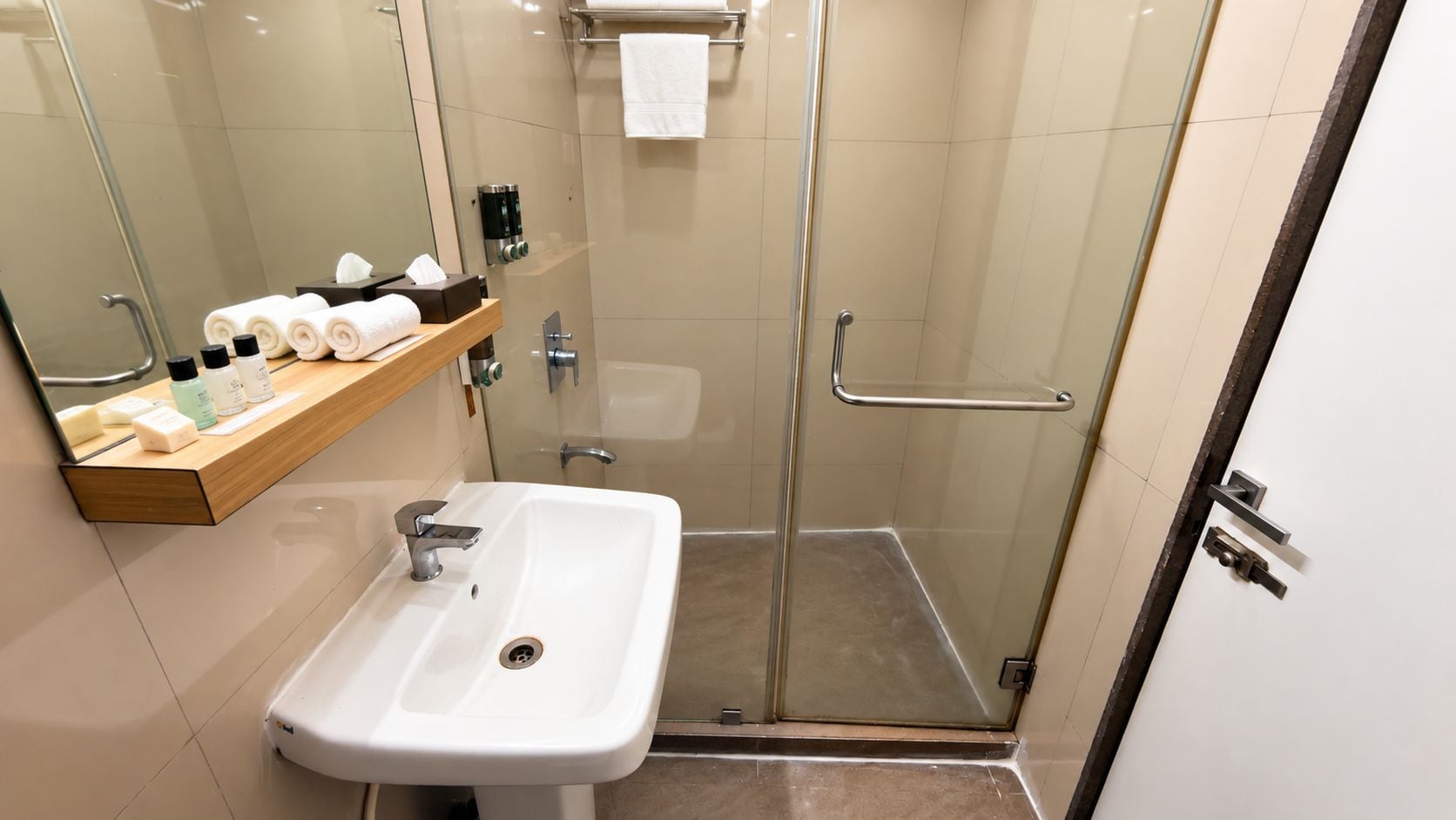 Un baño moderno con ducha de vidrio, un lavamanos con espejo y un estante con artículos de aseo.