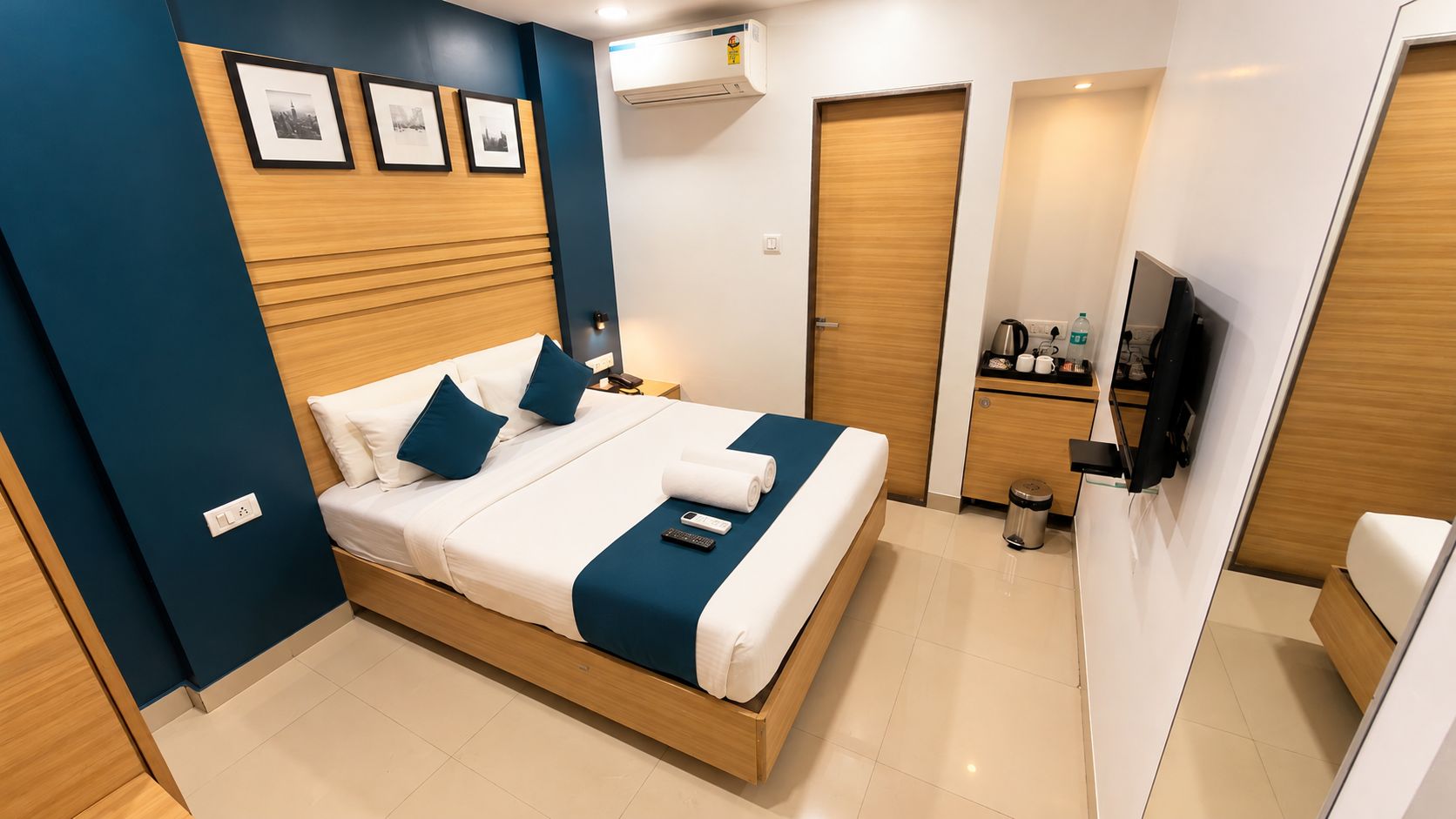 Een hotelkamer met een bed, nachtkastje, wandgemonteerde airconditioning, een televisie en een klein kitchenette.