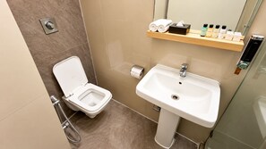 Casa de banho moderna com sanita, lavatório e prateleira com artigos de higiene pessoal.