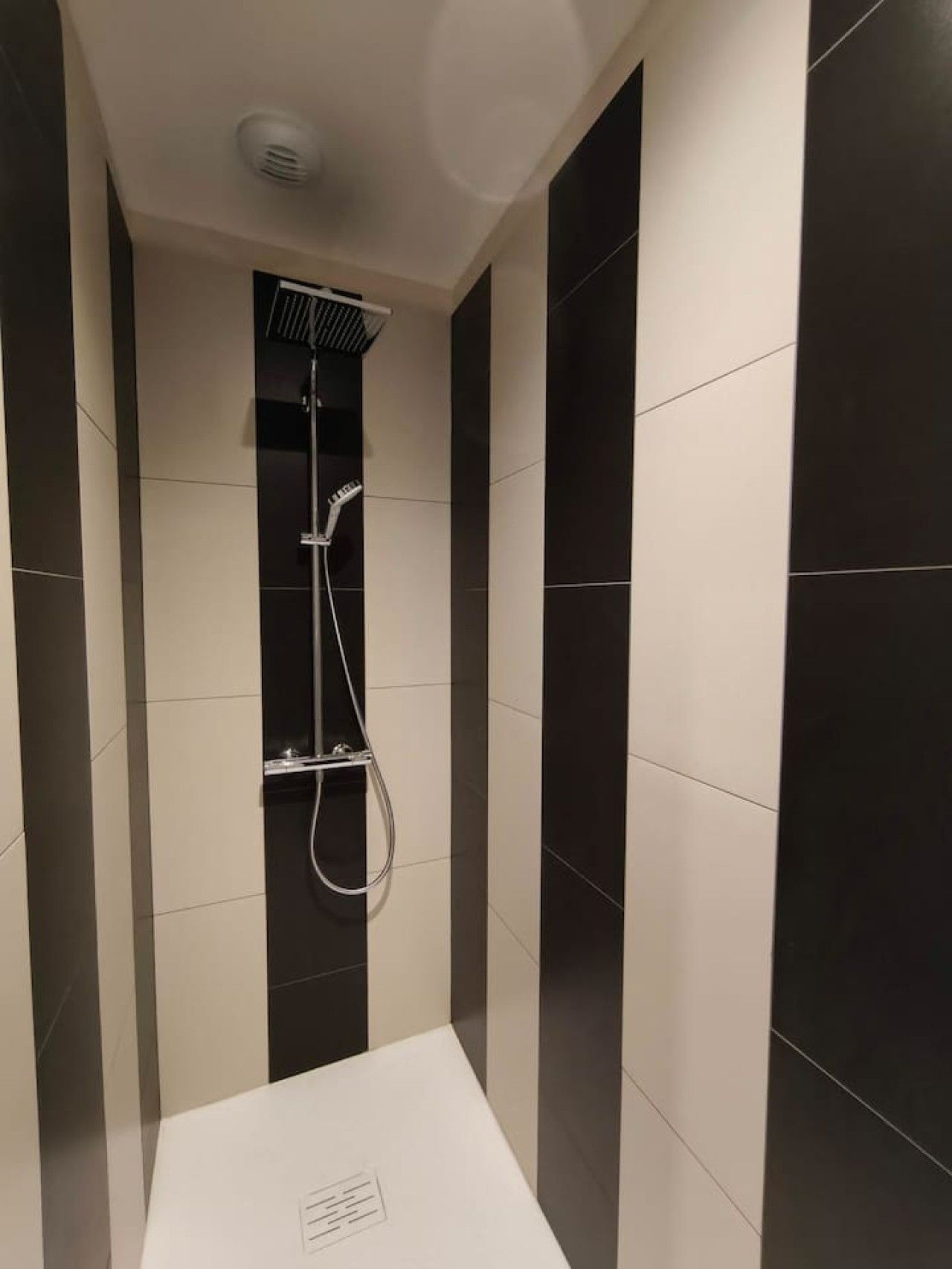 Une douche moderne dotée d’un pommeau de douche à main et d’un robinet mural.