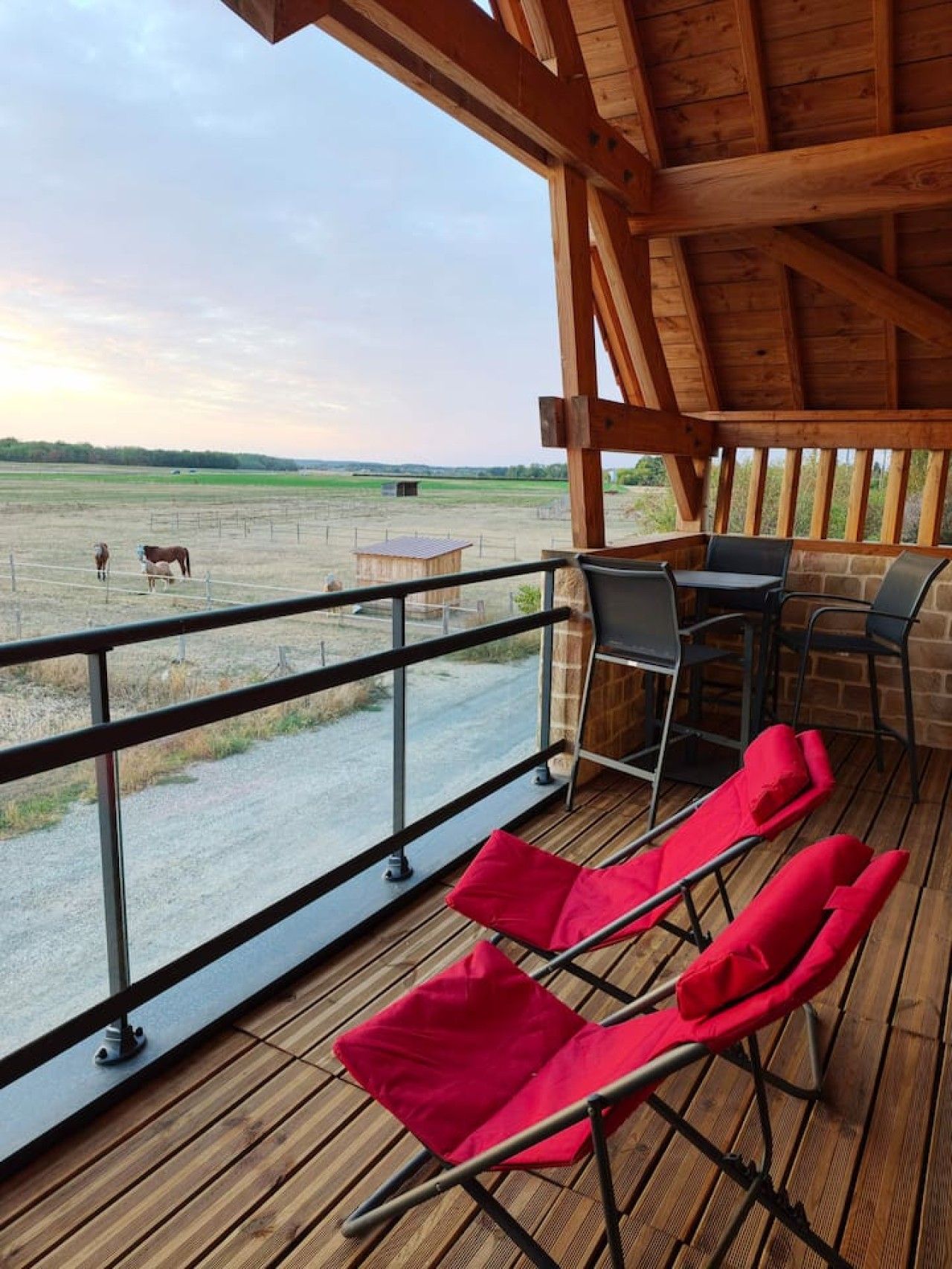 Un espace extérieur abrité doté d’une terrasse en bois, d’une rambarde en métal et de chaises longues rouges.