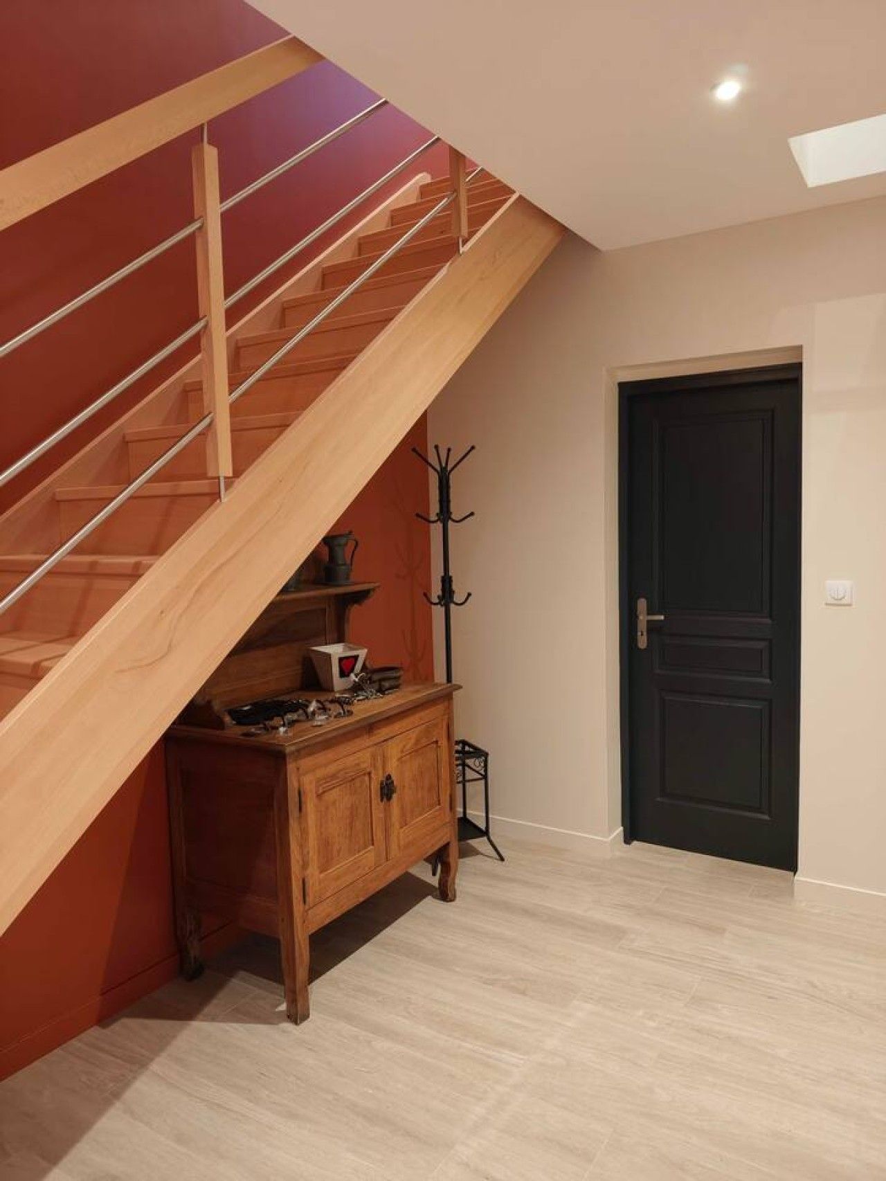 Un escalier avec des rampes en bois menant à l’étage supérieur, une porte sombre et un meuble en bois sur lequel sont posés divers objets.
