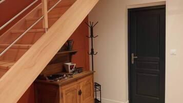 Un escalier avec des rampes en bois menant à l’étage supérieur, une porte sombre et un meuble en bois sur lequel sont posés divers objets.