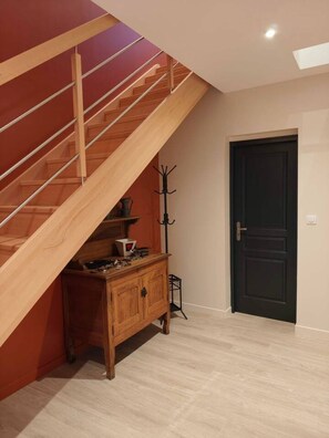 Eine Treppe mit Holzgeländern führt zu einer oberen Etage, ein dunkles Türelement und ein Holzschrank mit verschiedenen Gegenständen.
