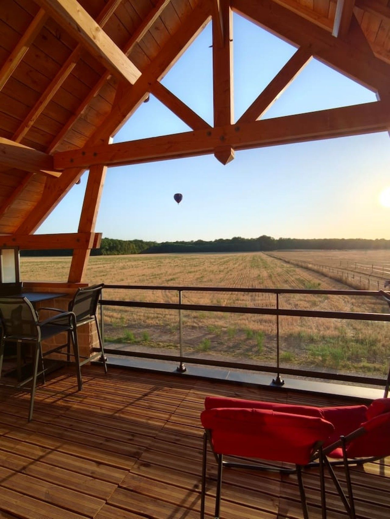 Une terrasse en bois offrant une vue sur un champ et sur une montgolfière au loin.