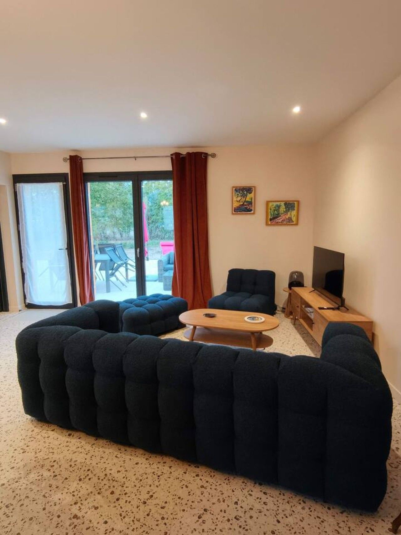 Un salon comprenant un grand canapé d’angle, une table basse en bois, un meuble pour la télévision et une porte-fenêtre coulissante donnant sur un espace extérieur.