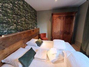 Una habitación de hotel con una cama, almohadas, cabecera de madera, una silla roja y un armario.