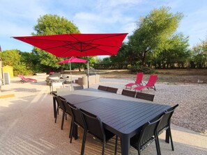 Un área de comedor al aire libre con una mesa, sillas, una parrilla y sombrillas rojas.