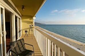 A balcony with a chair and a tripod, overlooking a beach with a clear sky. - Ocean Haven | Beachfront Getaway by Redondo Pier (Redondo Beach)