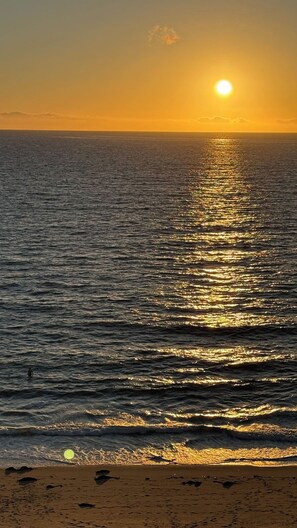 Un atardecer sobre un mar tranquilo con una playa al frente.