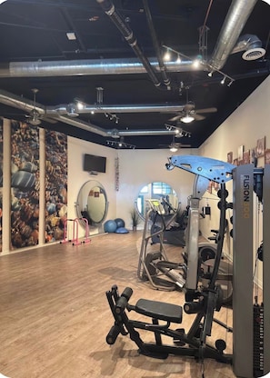 Un gimnasio con equipo de ejercicio, suelo de madera y un espejo circular en la pared.
